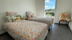 Ein Schlafzimmer mit zwei Betten, einem Sessel und einem Fenster mit Blick auf Bäume.
