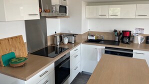 Eine moderne Küche mit weißen Schränken, einer schwarzen Induktionskochplatte, einem Edelstahl-Wasserkocher, einem Toaster, einer Kaffeemaschine und einem Geschirrspüler.