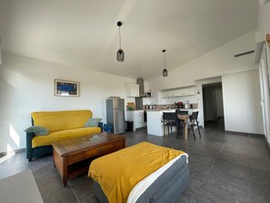A modern living room with a sofa, a coffee table, and a bed. There is a kitchen area with cabinets and a dining table. - Argelès Beach New 2BR - Balcony, Parking, Air Conditioning (Argelès-sur-Mer)