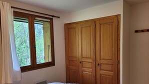 A bedroom with a bed, a window with curtains, and a wooden wardrobe. - Spacious T4 with garage and parking in Grand-Bornand - 6 pers (Le Grand-Bornand)