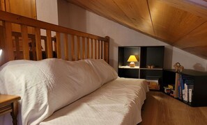 Ein Schlafzimmer mit einem hölzernen Bett, einem Nachttisch, einem Regal mit Büchern und einer Lampe.