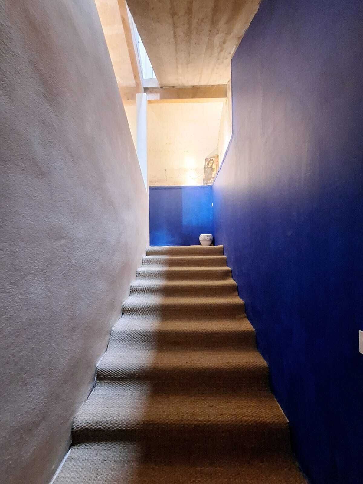 Uma escadaria estreita com degraus revestidos a carpete, que dá acesso a um patamar.
