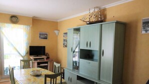 A dining area with a table and chairs, a television, and a cabinet with a ship model on top. - Cozy apartment in Pontaillac - 4 guests (Royan)