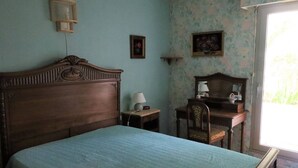 A bedroom with a wooden bed, a bedside table with a lamp, a chair, and a desk with a mirror. - Cozy apartment in Pontaillac - 4 guests (Royan)