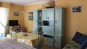 A room with a dining table, chairs, a television, a cabinet, and a sofa. - Cozy apartment in Pontaillac - 4 guests (Royan)