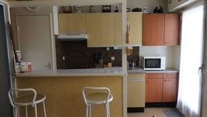 A compact kitchen with a microwave, wooden cabinets, and two bar stools. - Cozy apartment in Pontaillac - 4 guests (Royan)