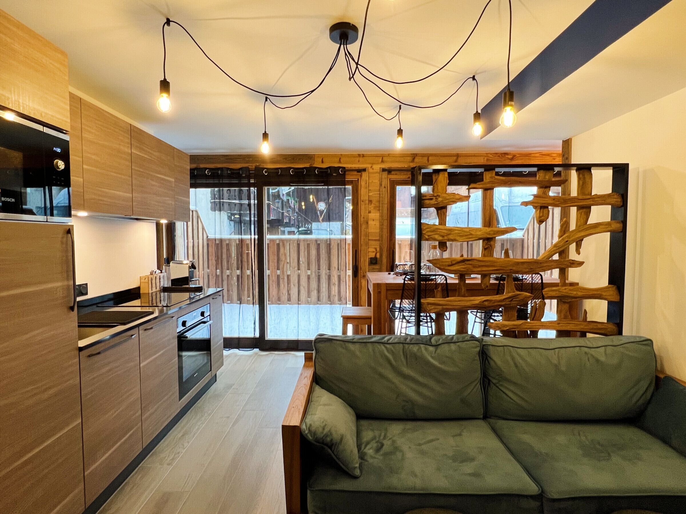 Una cocina moderna con armarios de madera, un refrigerador Bosch y un comedor con una mesa y sillas de madera.