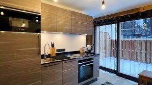 A modern kitchen with wooden cabinets, a Bosch microwave, a sink, and a built-in oven. There is a window with a view of a wooden deck outside. - Charming apartment in Les Gets, 2 bedrooms, Wi-Fi, parking included (Les Gets)