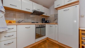 A compact kitchen with white cabinets, a stove, oven, and a coffee maker. - 2 bedroom lovely apartment in Vir (Vir)