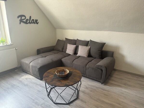 Un soggiorno moderno con un divano angolare grigio, un tavolino rotondo e un cartello appeso al muro con la scritta "Relax".
