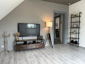 Un soggiorno moderno con TV a schermo piatto, una lampada, un tavolino consolle e una libreria.
