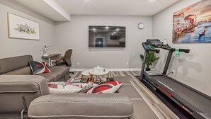 A modern living room with a sofa, ottoman, treadmill, and a painting of a cityscape. - Cozy and Tastefully Furnished 1BR Guest Suite Close to Spruce Meadows SW Calgary (Calgary)