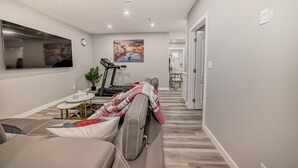 A modern living room with a sofa, a treadmill, and a painting on the wall. - Cozy and Tastefully Furnished 1BR Guest Suite Close to Spruce Meadows SW Calgary (Calgary)