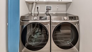 A laundry room with two stainless steel front-loading washing machines, a blue drying rack, and a white cabinet above. - Cozy and Tastefully Furnished 1BR Guest Suite Close to Spruce Meadows SW Calgary (Calgary)