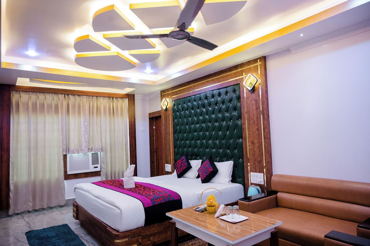 A hotel room with a bed, a sofa, a coffee table, a ceiling fan, and an air conditioning unit.