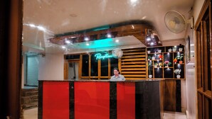 Un área de recepción con un letrero de neón, un mostrador de madera y un ventilador de pared.