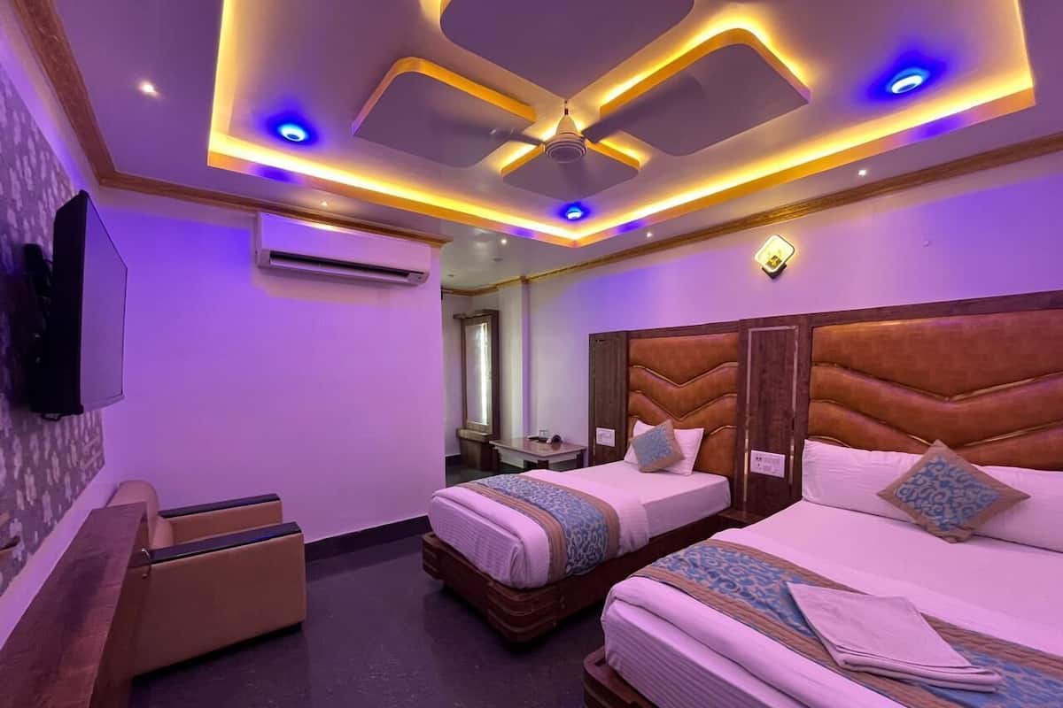 A hotel room with two beds, a flat-screen TV, a sofa, and a ceiling with recessed lighting.