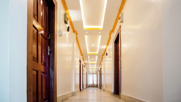Un largo y estrecho pasillo de hotel con puertas de madera a ambos lados, iluminación empotrada y suelo de mármol.
