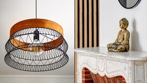 A modern pendant light with a geometric wire frame and a wooden shade, a Buddha statue on a white marble pedestal, and vertical wooden slats in the background. - Appartment aux Champs-Elysées avec climatisation (Paris)