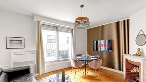 A modern living room with a sofa, a dining table with chairs, a fireplace, a TV, and a large window with curtains. - Appartment aux Champs-Elysées avec climatisation (Paris)