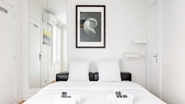 A modern hotel room with a large bed, white walls, a framed artwork, and a wardrobe. - Appartment aux Champs-Elysées avec climatisation (Paris)