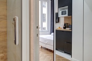 Una habitación moderna con una cama, una zona de cocina con microondas y vistas al balcón exterior.