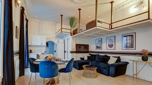 A modern living room with a black sofa, blue chairs, a dining table, and a kitchen in the background.
