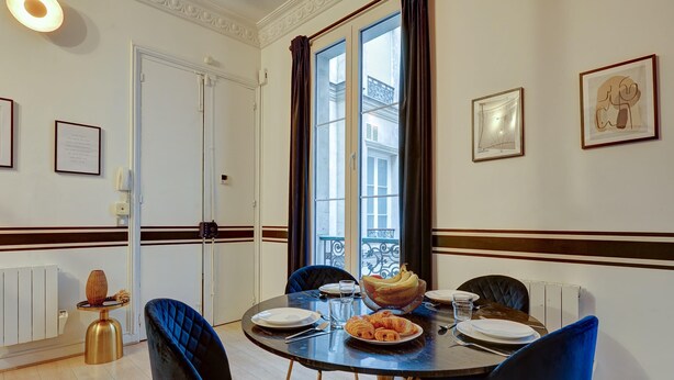 A dining area with a round table, blue chairs, and a basket of croissants.
