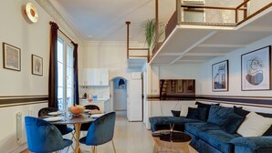A modern living room with a blue sofa, a dining table with chairs, and a kitchen in the background.
