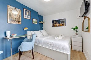 Une chambre à coucher moderne avec un lit, un bureau, une chaise, une table de chevet agrémentée d’une plante et des œuvres d’art mural.