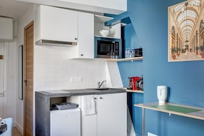 Une cuisine compacte équipée d’un four à micro-ondes, d’un évier et d’un petit réfrigérateur. Un mur d’accent bleu et une œuvre d’art encadrée ornent l’espace au-dessus du plan de travail.