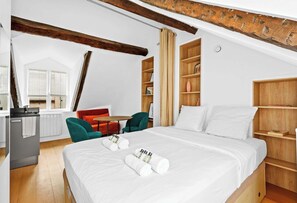 A hotel room with a bed, a desk, a chair, and a bookshelf.