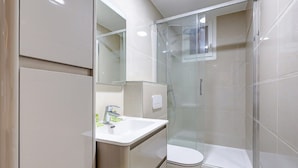 Un baño moderno con ducha envuelta en vidrio, un lavamanos blanco y un inodoro.