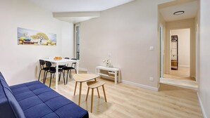 Una sala de estar moderna con un sofá azul, una mesa de comedor con sillas y una pequeña mesa blanca con un florero.