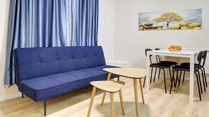 Una sala de estar con un sofá azul, una mesita de madera y una mesa de comedor blanca con sillas negras.