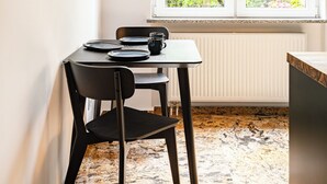 A dining area with a table and chairs, a window with a view of greenery, and framed artwork on the wall. - RentPlanet - Apartament Grabiszyńska (Wroclaw)