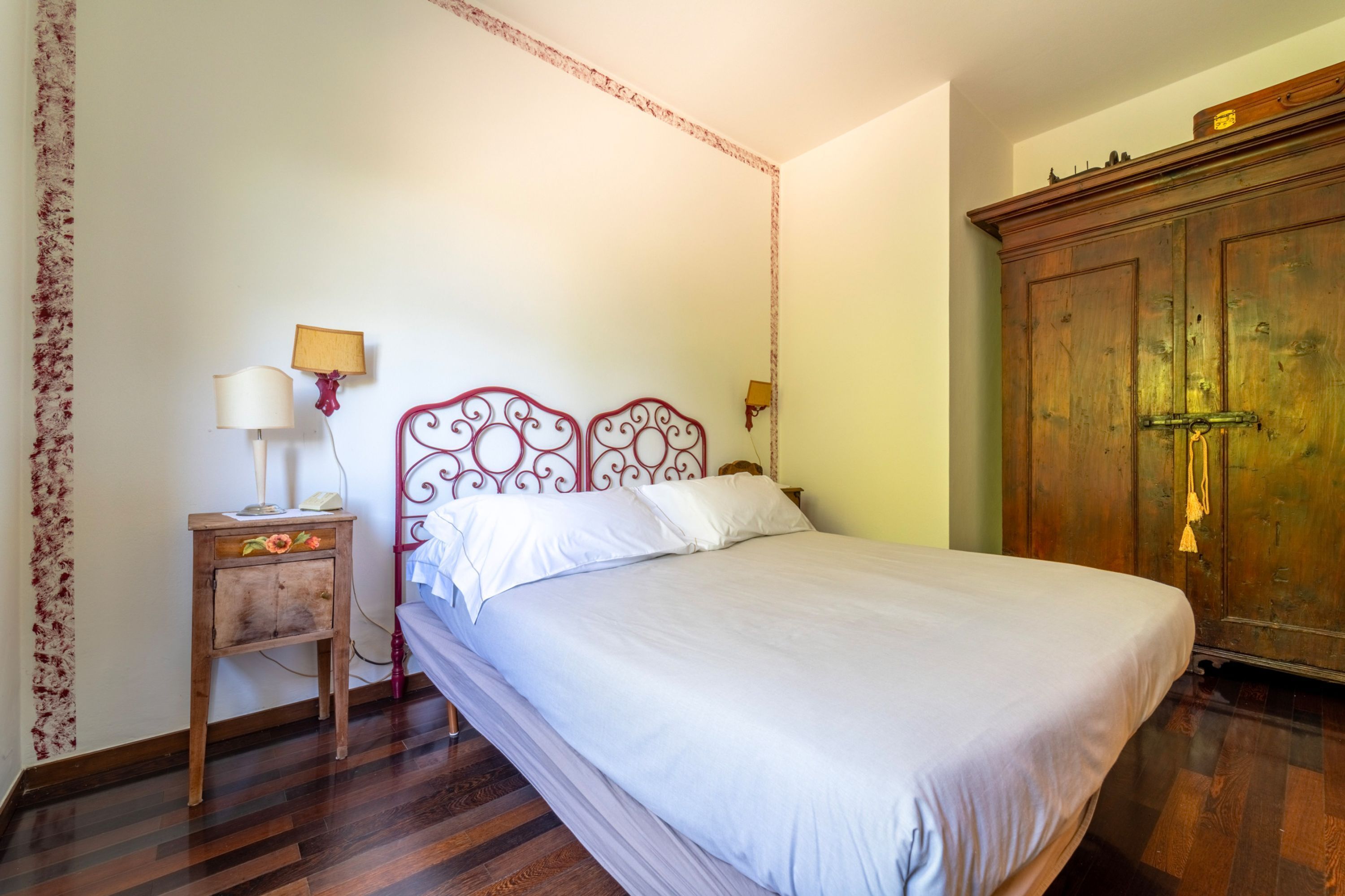A bedroom with a bed, a wooden nightstand, a lamp, and a wardrobe.