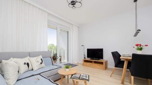 A modern living room with a sofa, a TV, a dining table, and a bookshelf. - Spacious Apartment in Wola | Parking | Balcony (Warszawa)