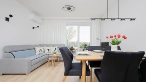 A modern living room with a grey sofa, black chairs, a wooden dining table, and a vase of red tulips. - Spacious Apartment in Wola | Parking | Balcony (Warszawa)