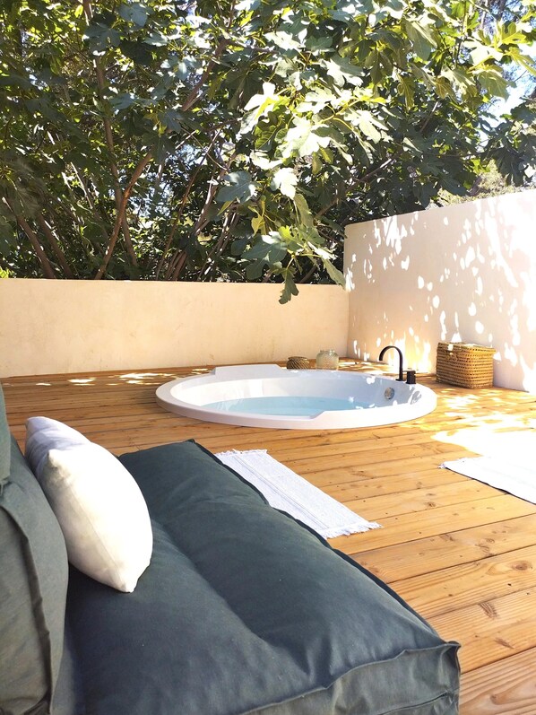 Una terraza de madera con un jacuzzi, un sofá verde y una pared con un árbol.