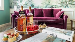 A table with a bottle of Bacardi, a bottle of Disaronno, and glasses of red wine, along with a magazine titled "Magical Venice" and a tray of appetizers.