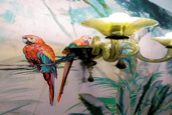 A mural of colorful parrots on a wall with a chandelier.