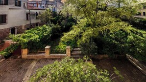A courtyard with a stone wall, lush greenery, and buildings in the background.