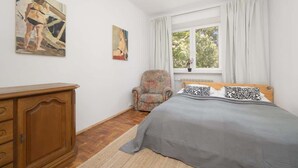 A bedroom with a bed, a wooden dresser, a chair, and two paintings on the wall.