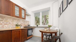 A kitchen with wooden cabinets, a brick backsplash, a window with a view of trees, and a round table with chairs.