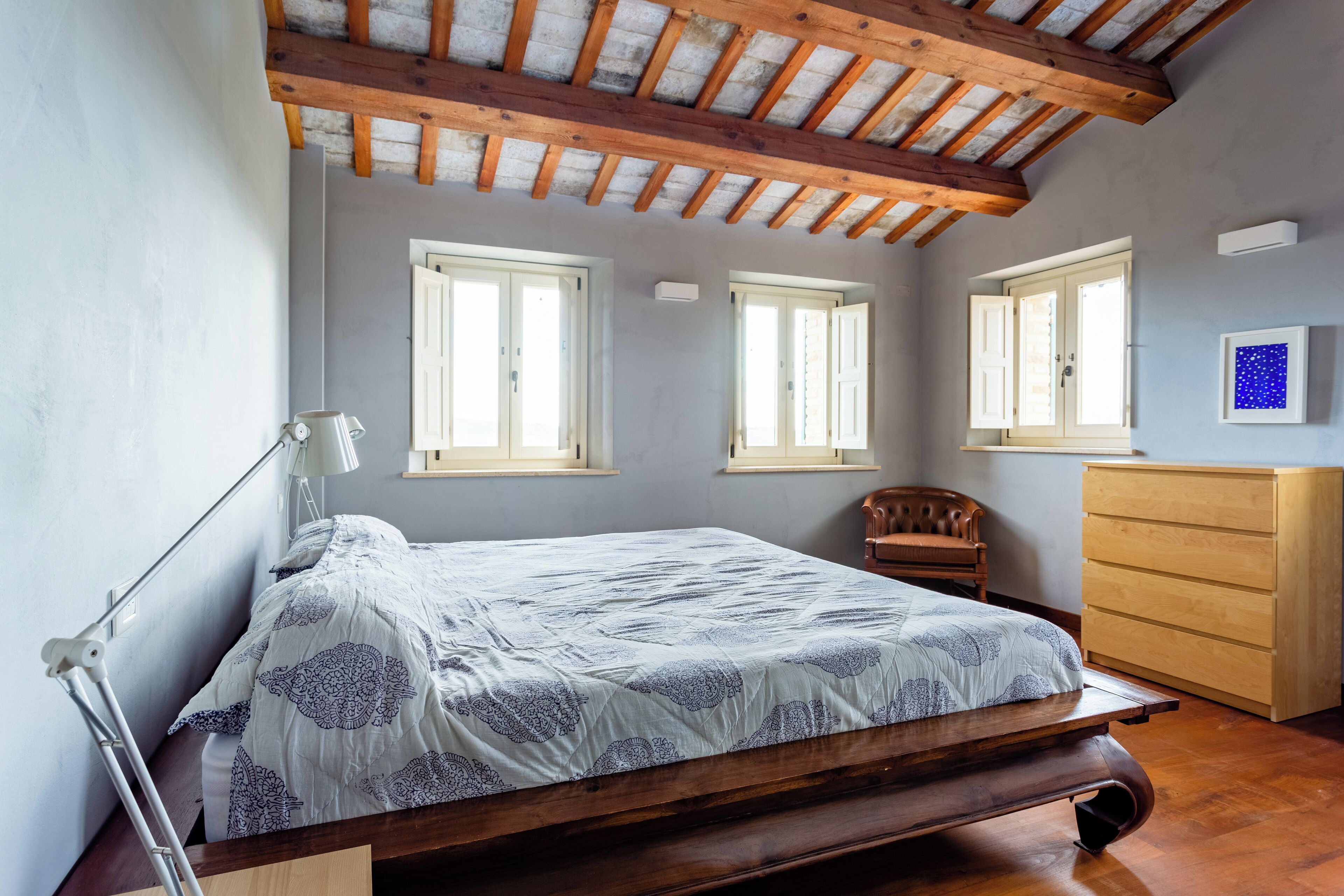 A bedroom with a wooden bed, a desk, a chair, a dresser, and a window with a view of the outside.