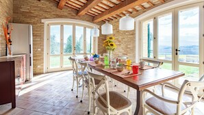 A spacious kitchen with a long wooden table, white chairs, and a view of the outdoors through large windows. - Elegant typical farmhouse with pool large wooded courtyard 10 minutes from Jesi (Marche)