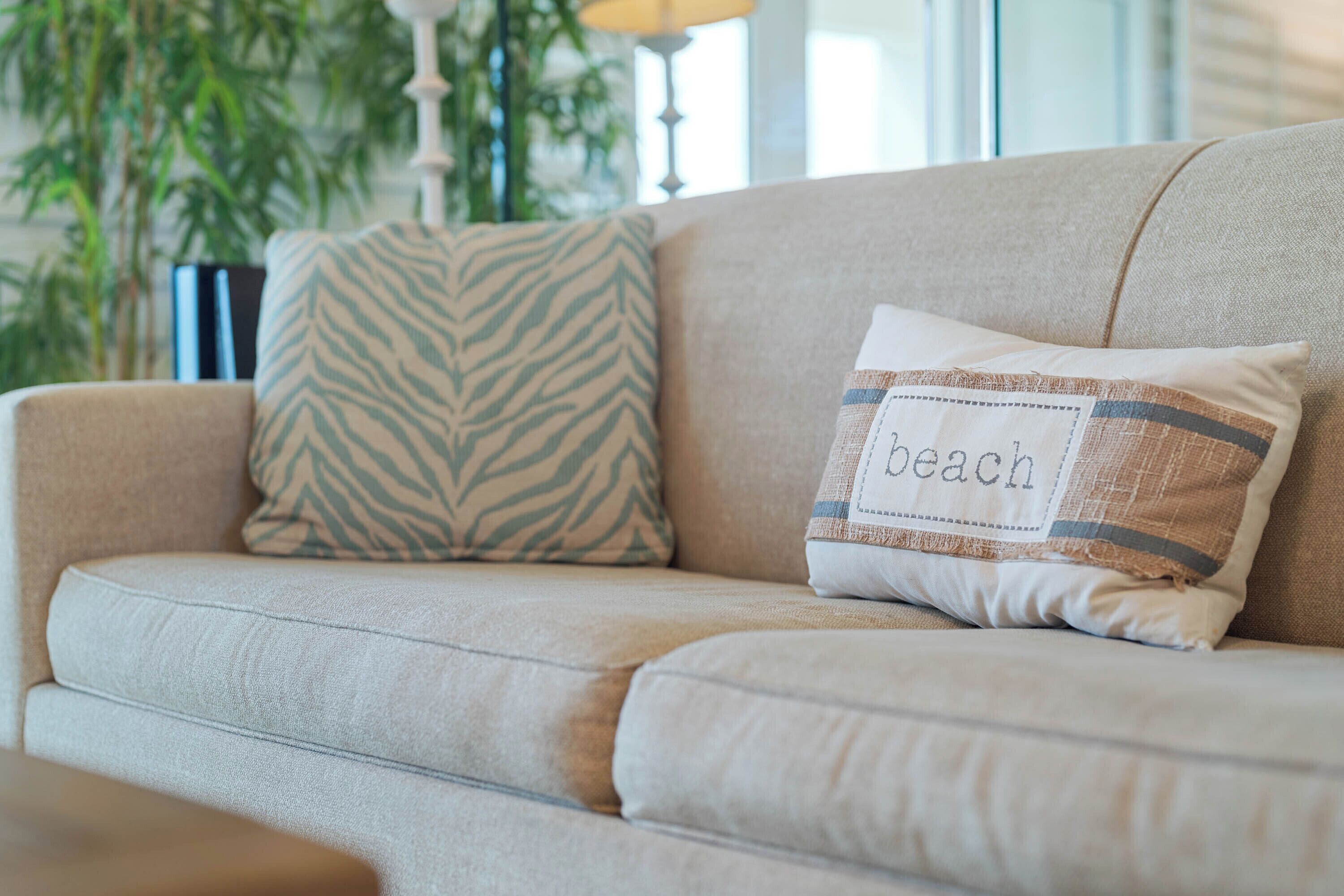 Un canapé beige agrémenté d’un coussin à motifs zébrés et d’un autre coussin sur lequel est écrit le mot « plage ».