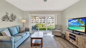 A living room with a sofa, coffee table, TV, and a view of a balcony with outdoor furniture.