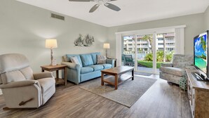 A living room with a sofa, armchairs, a coffee table, a TV, and a ceiling fan.